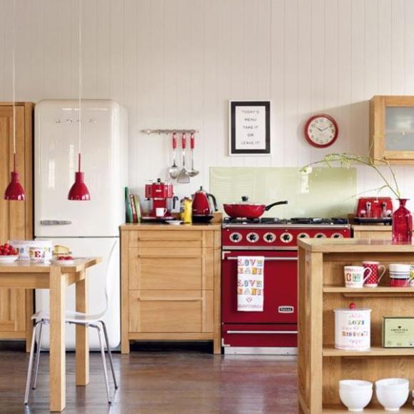 Красный цвет техники и посуды удачно подчеркивает ретро-стиль кухни из светлого дерева.